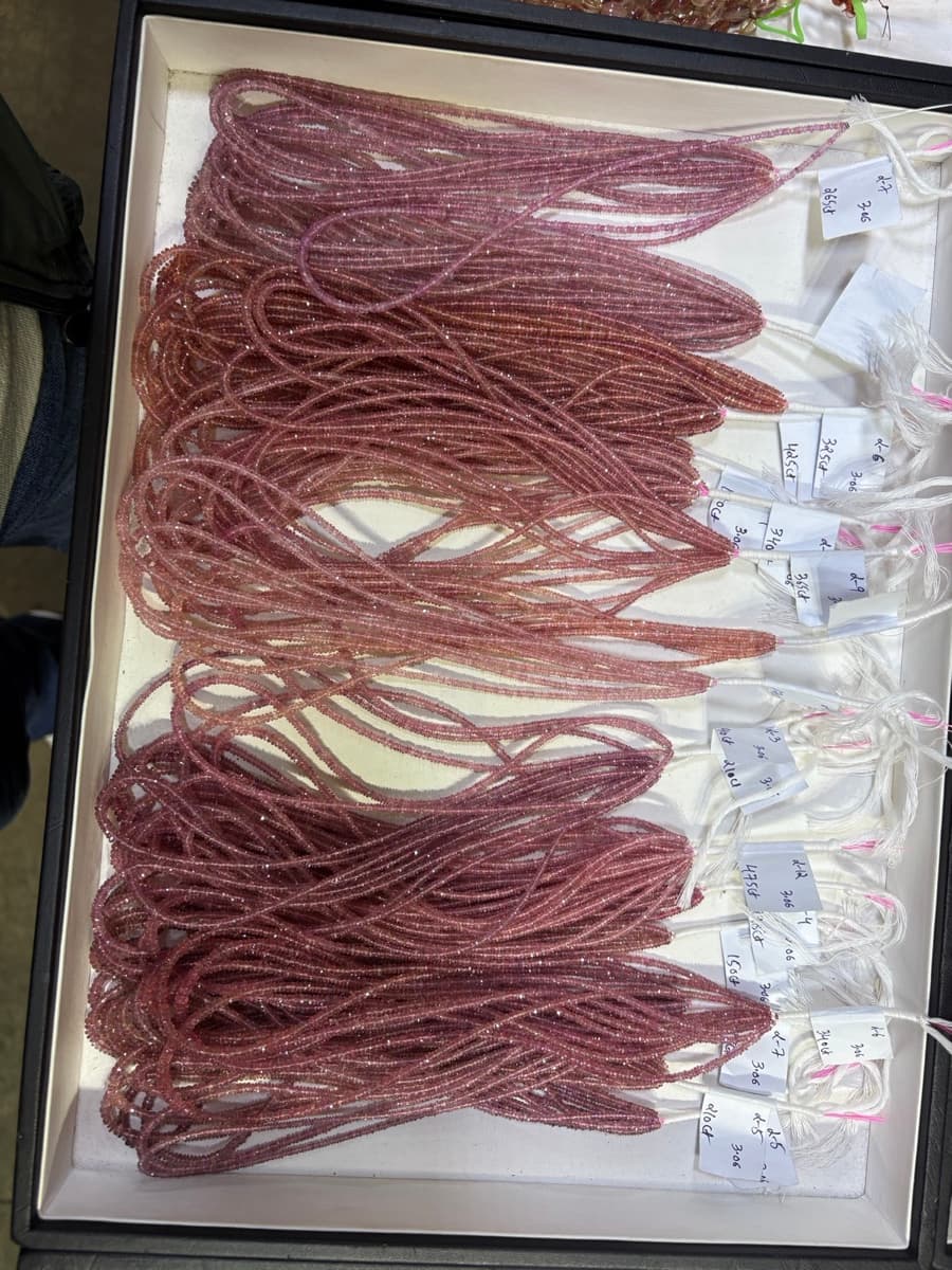 Tray of pink sapphire bead strands with tags